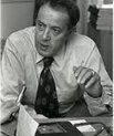 Black and white photo of a man in a white shirt and a tie speaking at a meeting