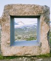 A large square frame made from stone. Its inside edges are perfectly even, while the outside edges are uneven stone. Placed high up in the mountains and hills.