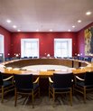 A meeting room with a large round table with chairs around it in the centre. 