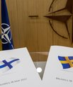 Two documents, one with the Finnish flag and one with the Swedish flag, laying on a glass table in an official-looking office.