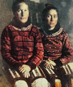 Old photo of two girls sitting beside each other in long red dresses with pattern