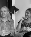 Black and white photo of two female academics sitting on a sofa discussing.